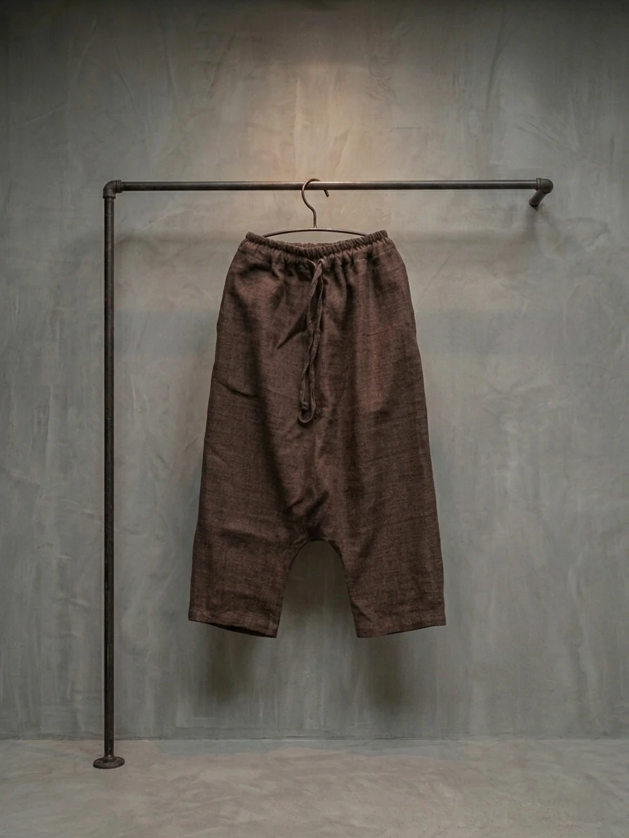 Wild Silk Low Crotch Trousers hanging on a metal rack against a concrete wall